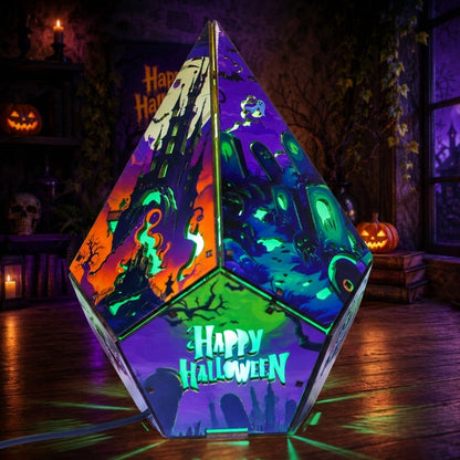 A large, geometric pyramid-shaped LED light with a Halloween theme, featuring colorful panels with haunted houses, ghosts, and spooky illustrations, and the words 'Happy Halloween' illuminated on the front. It is displayed on a wooden floor in a dimly lit, atmospheric Halloween room setting.